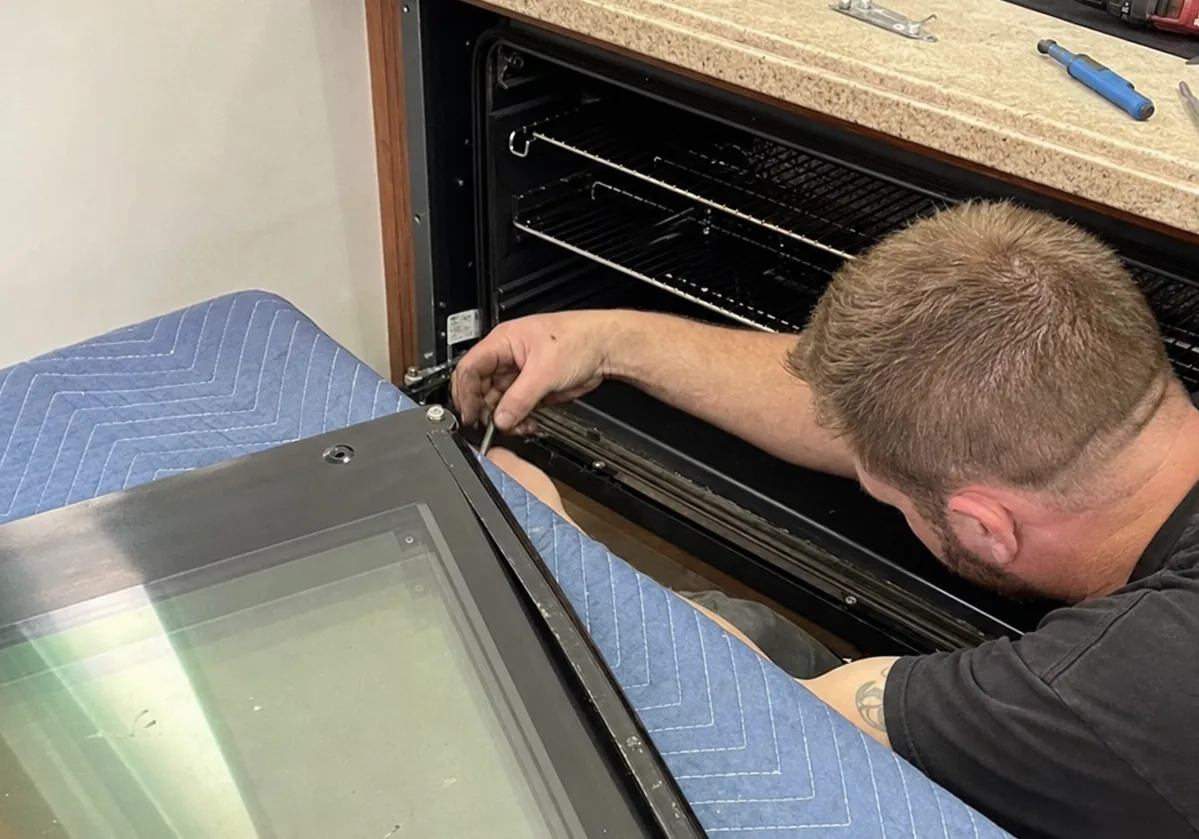 Close view into a stainless oven cavity with racks and rails visible and the door lying on a blanket alongside